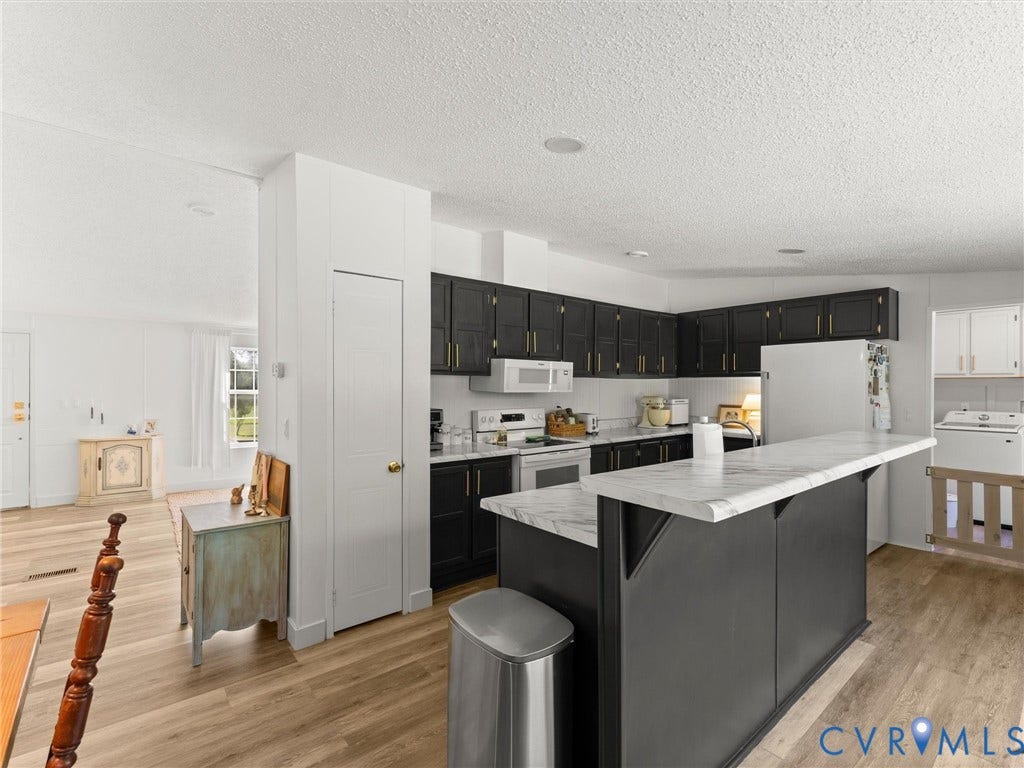 4554 Powhatan Lakes Road, Powhatan, VA 23139 Modern kitchen featuring black cabinetry with white countertops, a large center island with seating, stainless steel appliances, and warm wood-finish flooring throughout the open-concept space