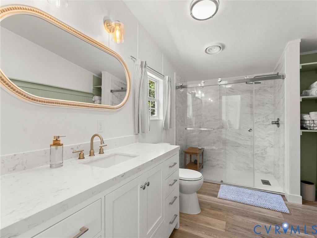 4554 Powhatan Lakes Road, Powhatan, VA 23139 Bathroom featuring a white vanity with a light-colored countertop, gold-finish fixtures, a framed mirror, and a glass-enclosed shower with tiled walls