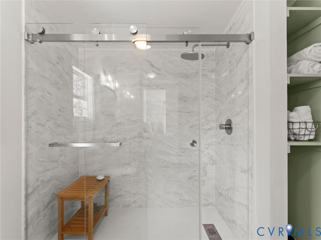 4554 Powhatan Lakes Road, Powhatan, VA 23139 Frameless glass shower enclosure with a rain shower head, textured shower wall panels, and built-in shelving