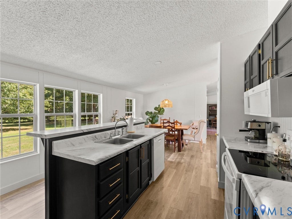 4554 Powhatan Lakes Road, Powhatan, VA 23139 Chef's kitchen featuring a center island with waterfall-edge countertop, dual sink, and black cabinetry with brass hardware