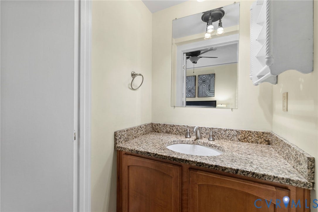 Built-in vanity with wood-finish cabinetry, granite-style countertop, and an undermount sink with a brushed nickel faucet