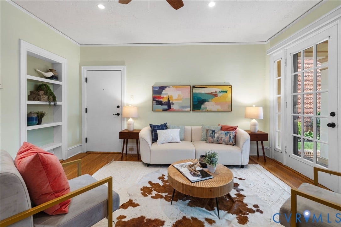 Hardwood flooring and crown molding accent this living space, featuring built-in shelving, a solid entry door, and French doors