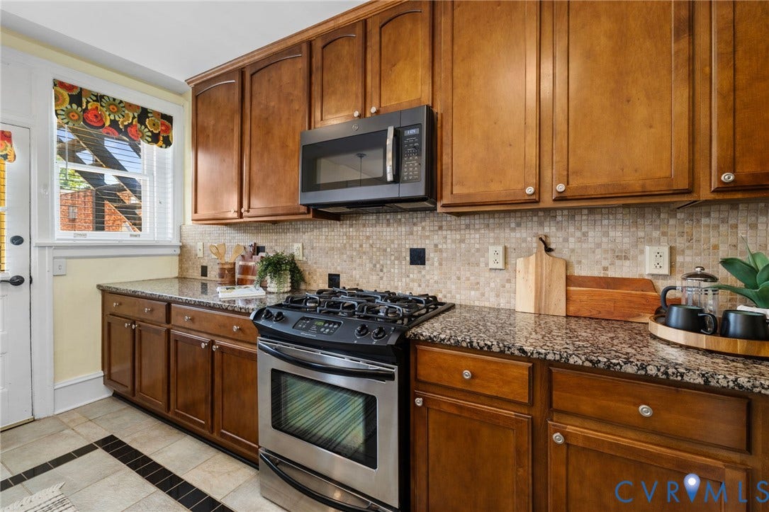 Wood-finish cabinetry, granite countertops, tile backsplash, and stainless steel gas range with microwave