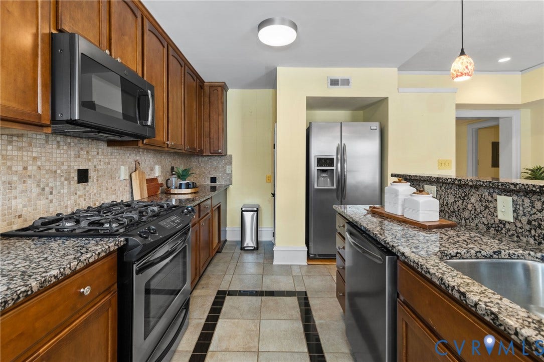 Wood-finish cabinetry, granite countertops, tile backsplash, and stainless steel gas range with microwave