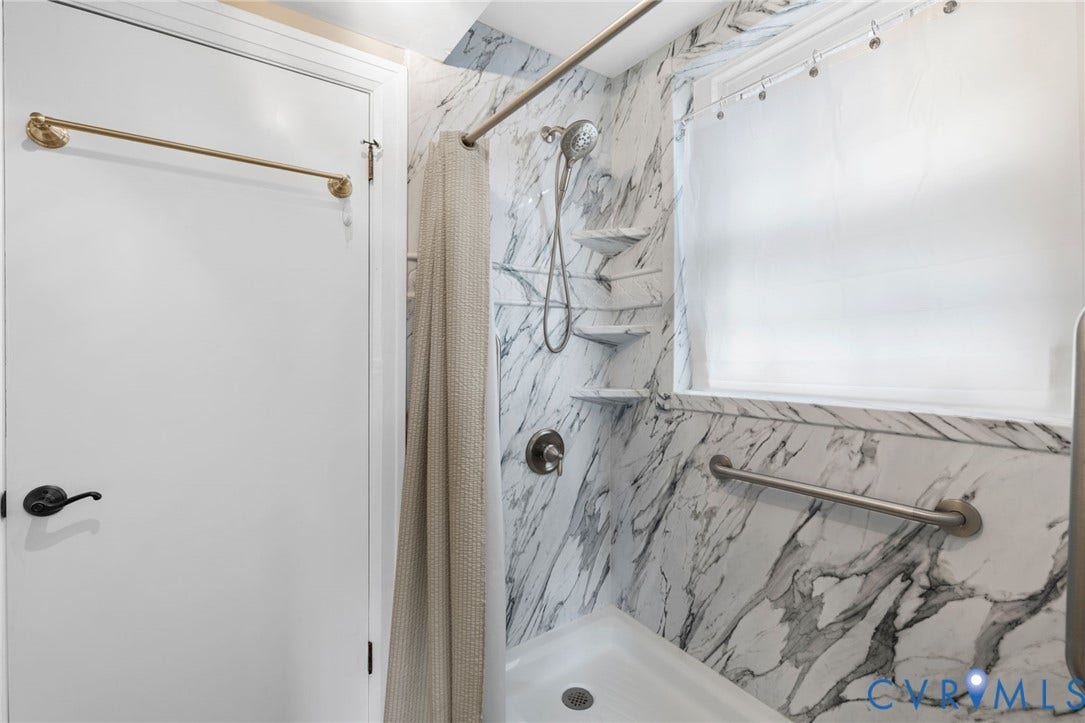 White and gray veined shower surround with corner shelving, a handheld shower fixture, and a built-in window