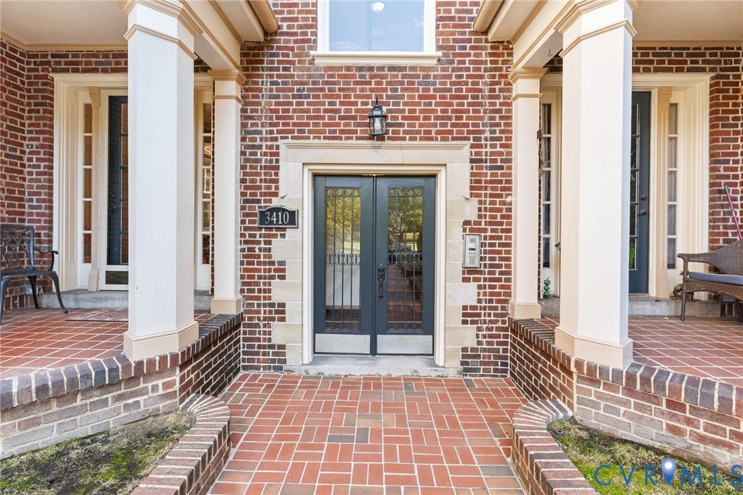 Brick exterior featuring stone accents, a brick paver walkway, and a covered porch with substantial columns