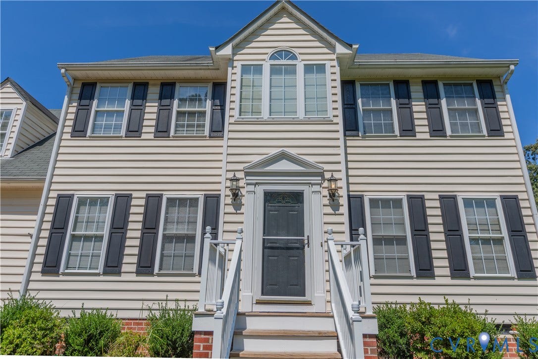 Two-story residence featuring light-colored siding, dark shutters, and a prominent front entry with an arched window above