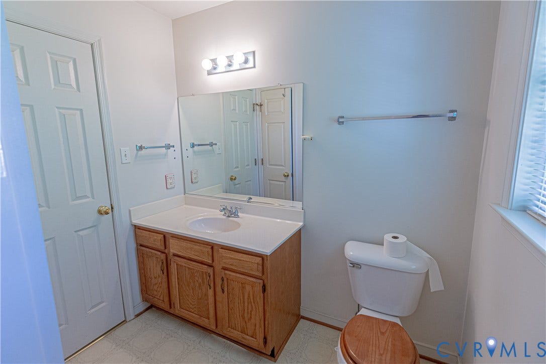 White vanity with integrated sink, wood-finish cabinetry, and overhead lighting