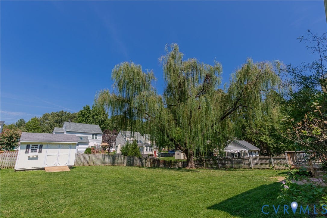 Expansive lawn featuring a mature weeping willow, storage shed with double doors, and a decorative gazebo