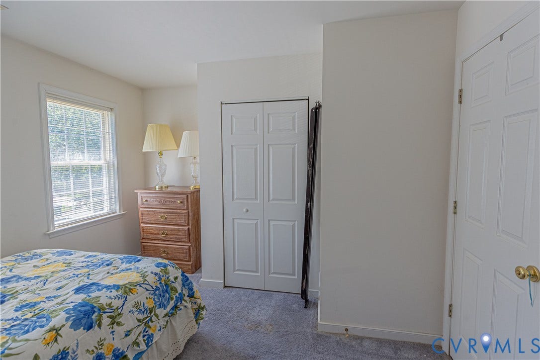 Carpeted flooring, white bi-fold closet doors, white paneled door with brass hardware, and a window with white trim
