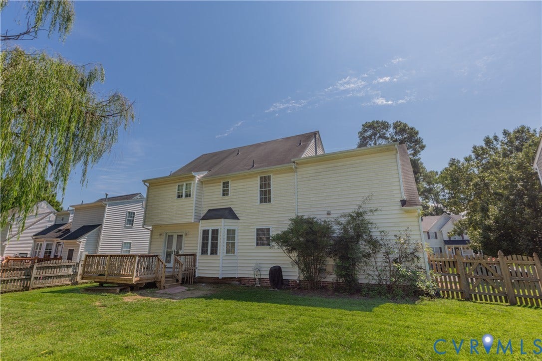 Expansive backyard featuring a manicured lawn, a wooden deck, and a picket fence