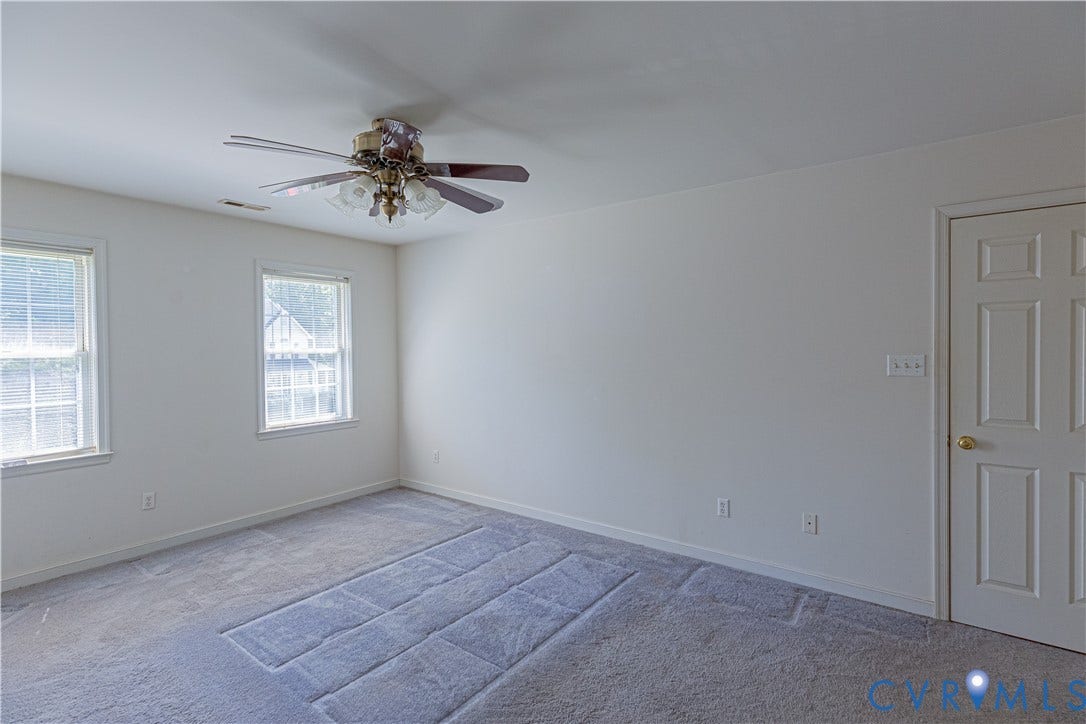 Two double-hung windows, ceiling fan with integrated lighting, paneled interior door, and wall-to-wall carpeting