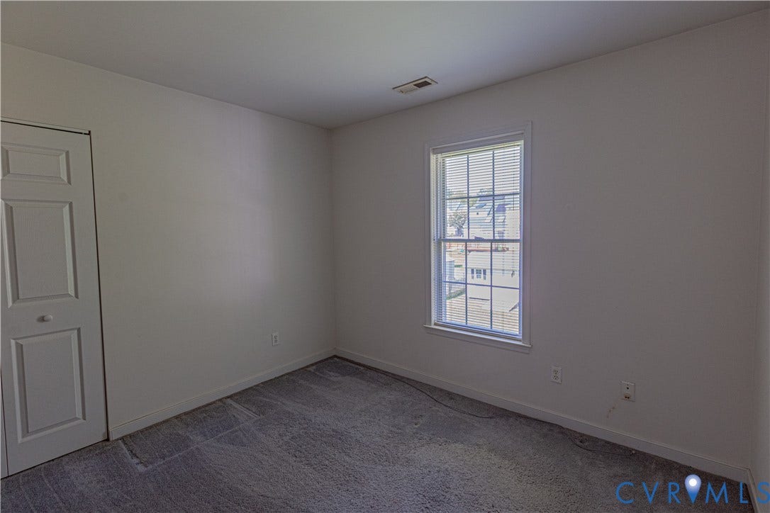 White interior walls, carpet flooring, and a single window with blinds