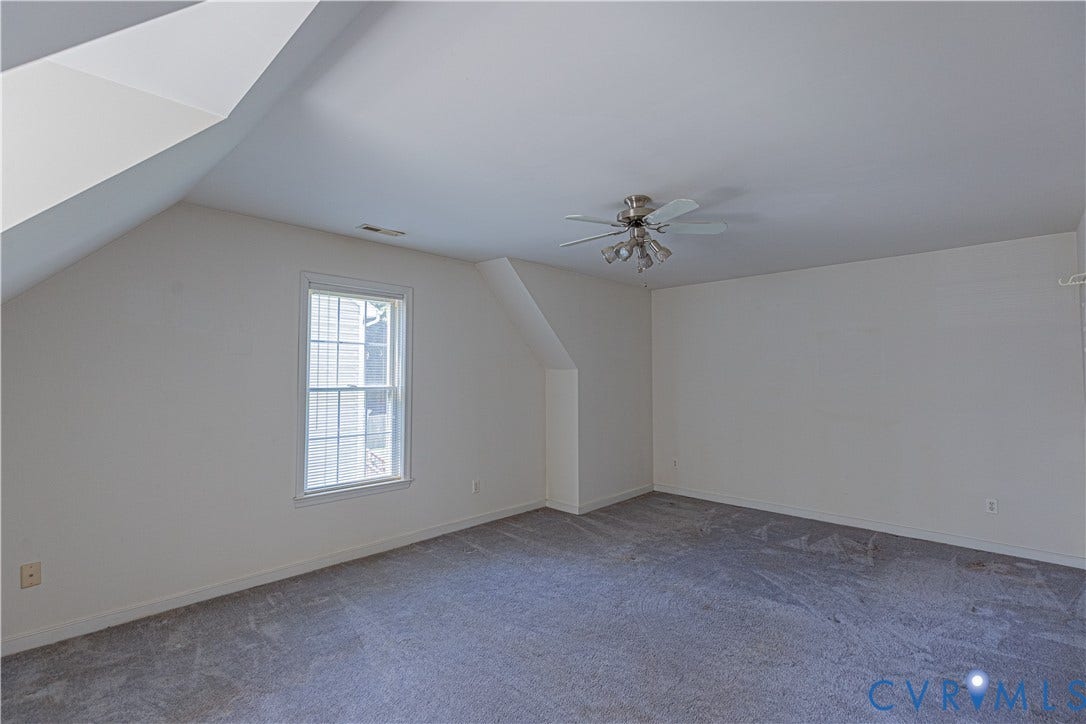 Carpeted flooring with a white window frame, sloped ceilings, and a ceiling fan