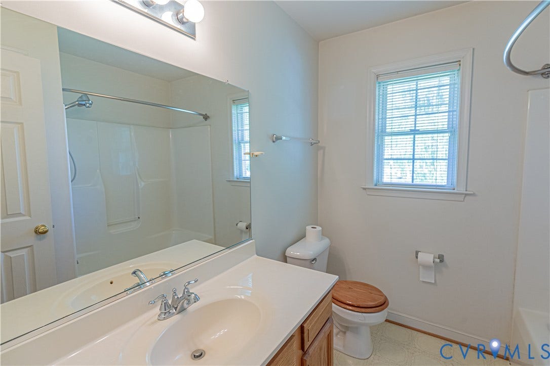 Bathroom featuring a white vanity with integrated sink, chrome faucet, wall-mounted mirror, and an adjacent window with blinds