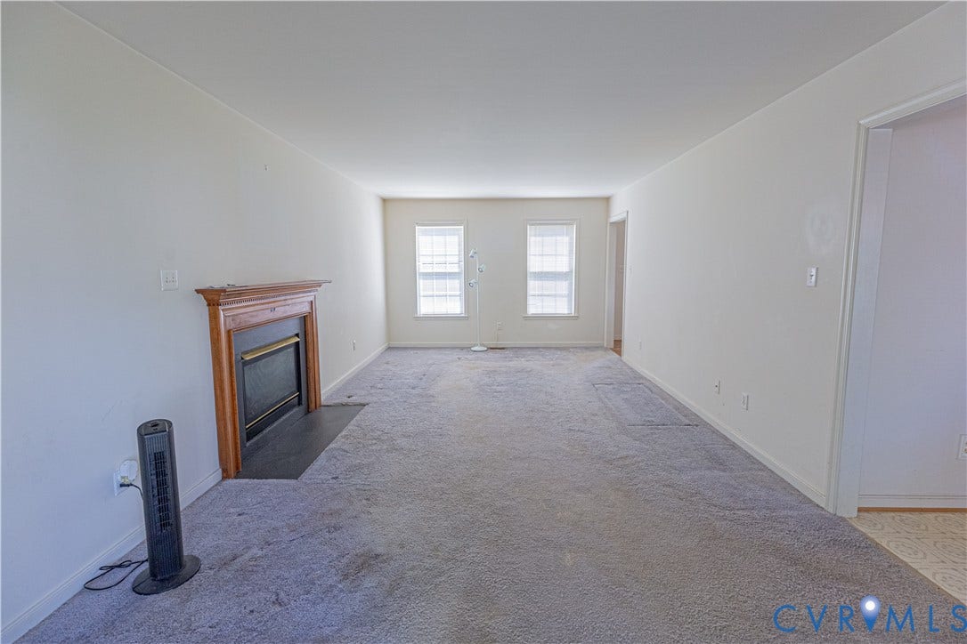 Neutral wall colors, wood-finish fireplace mantel with hearth, and two windows with blinds