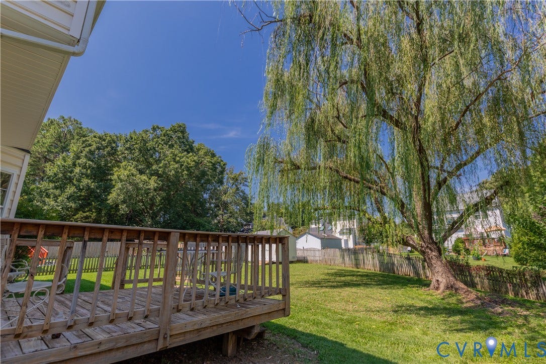 Expansive backyard featuring a wood deck, manicured lawn, and mature trees