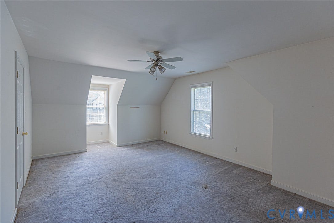Spacious room featuring sloped ceilings, two windows, wall-to-wall carpeting, and a ceiling fan
