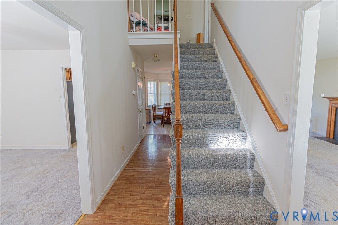 Foyer with wood-finish flooring, carpeted staircase, and white painted walls