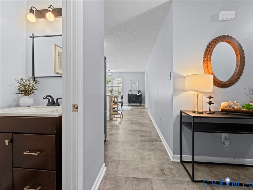 6712 N Hedges Road, Chesterfield, VA 23224 Hallway with durable flooring and light gray wall color, offering a glimpse into a bathroom with a dark wood vanity and a living space beyond