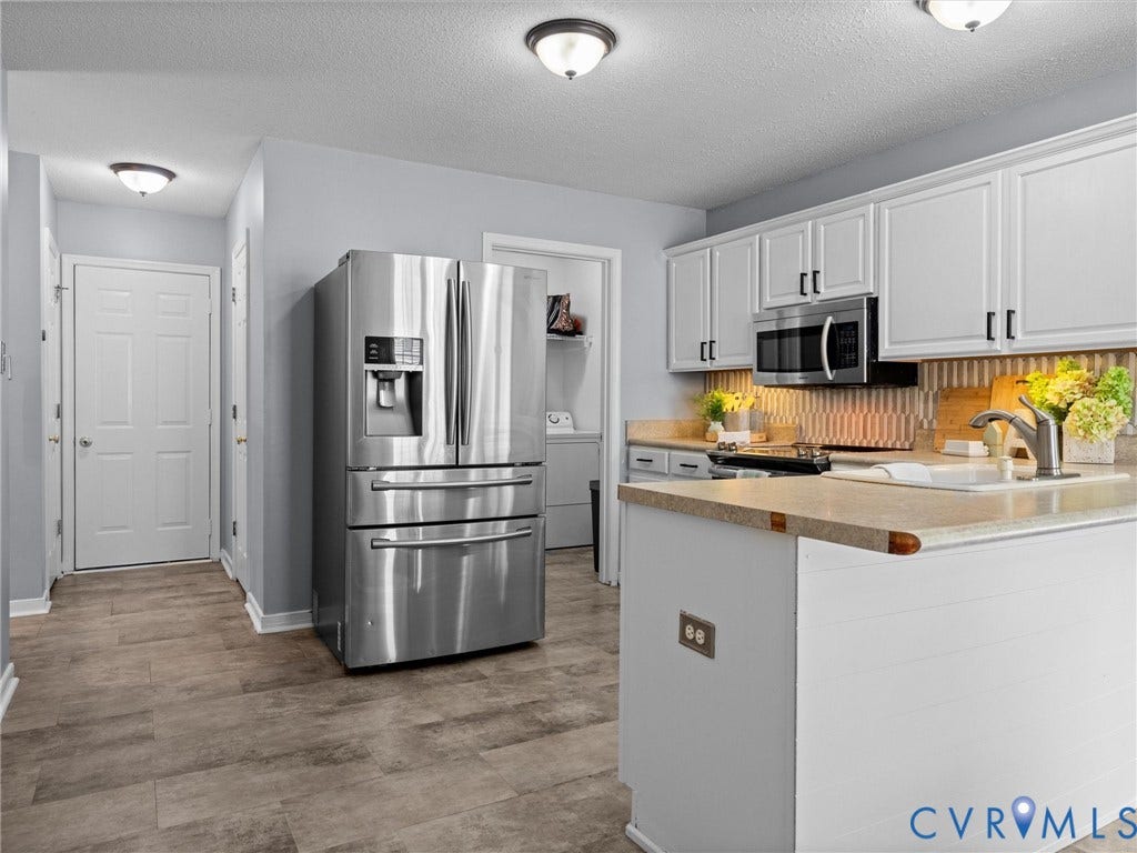 6712 N Hedges Road, Chesterfield, VA 23224 Kitchen featuring white cabinetry, stainless steel appliances, wood-finish flooring, a textured tile backsplash, and a kitchen island with a built-in sink