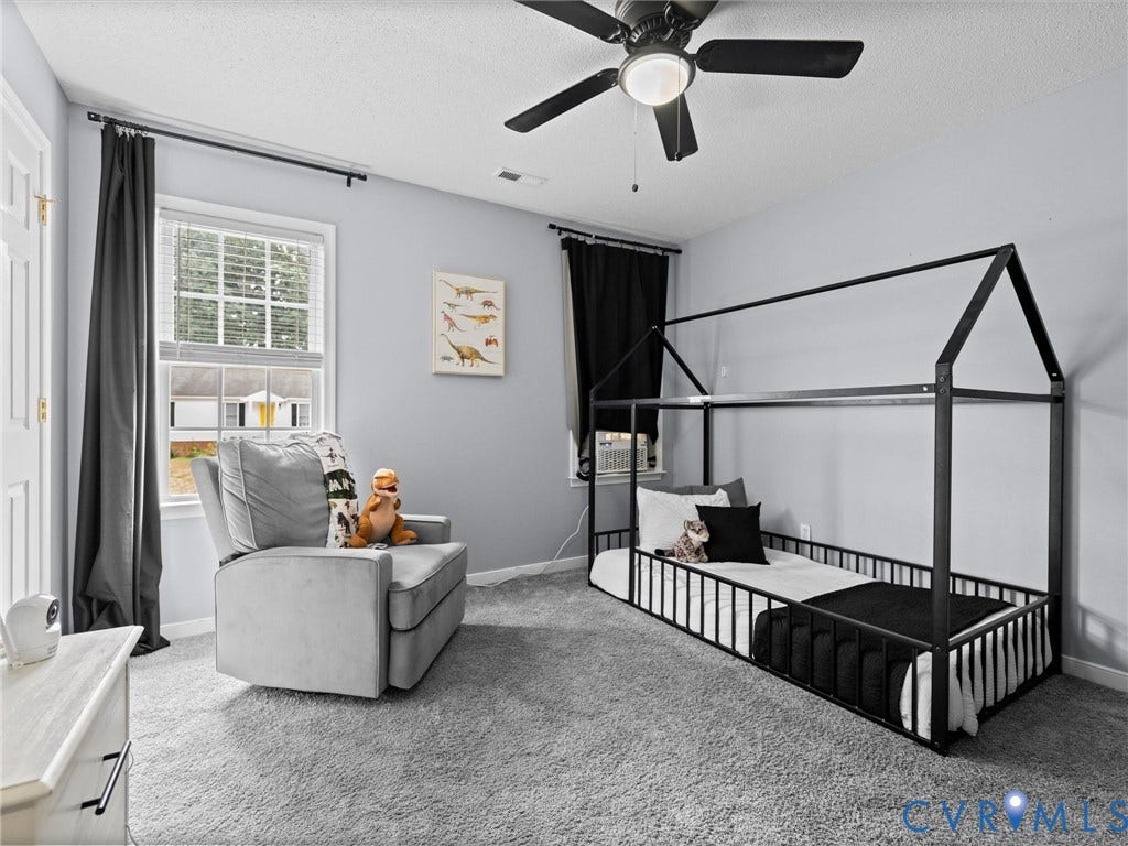 6712 N Hedges Road, Chesterfield, VA 23224 Spacious room featuring light gray walls, plush gray carpeting, a multi-pane window with blinds, a white door with gold-toned hardware, and a ceiling fan with integrated lighting