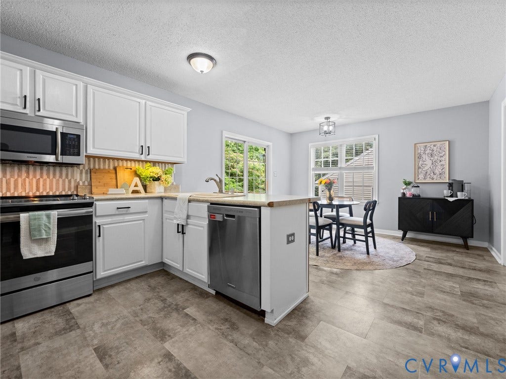 6712 N Hedges Road, Chesterfield, VA 23224 Open-concept kitchen and dining area featuring white cabinetry, stainless steel appliances, a tile backsplash, wood-finish flooring, and a sliding glass door