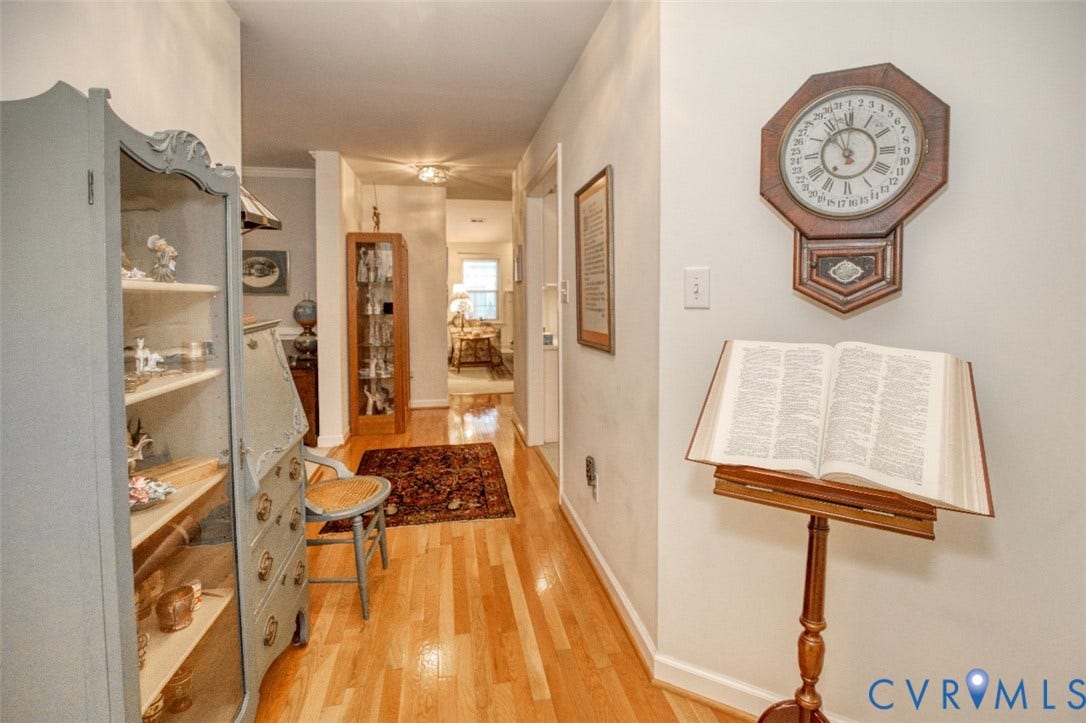 6311 Chiswick Park, Williamsburg, VA 23188 Charming hallway showcasing warm wood-finish flooring, white painted walls, and built-in cabinetry with glass-front doors