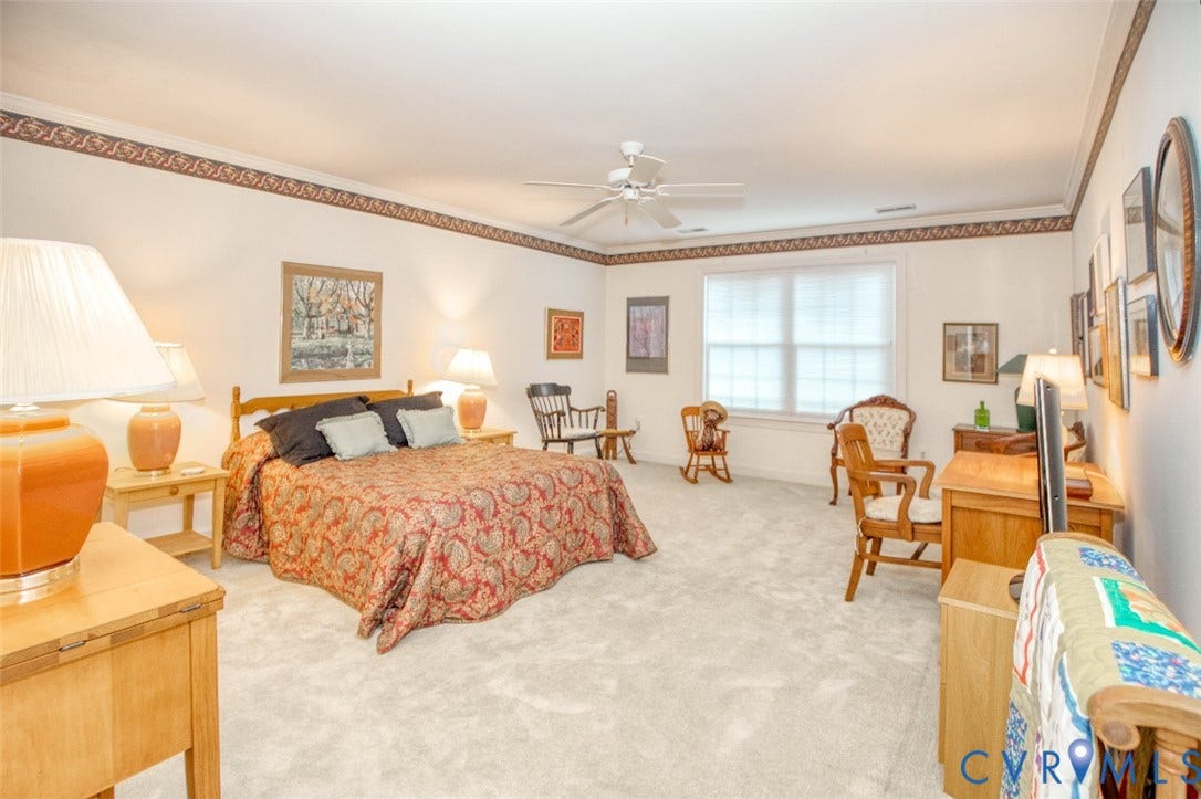 6311 Chiswick Park, Williamsburg, VA 23188 Spacious primary bedroom suite offering abundant natural light from multiple windows, wood-finish flooring throughout, decorative ceiling detail with crown molding, and ample room for bedroom furnishings and separate seating areas