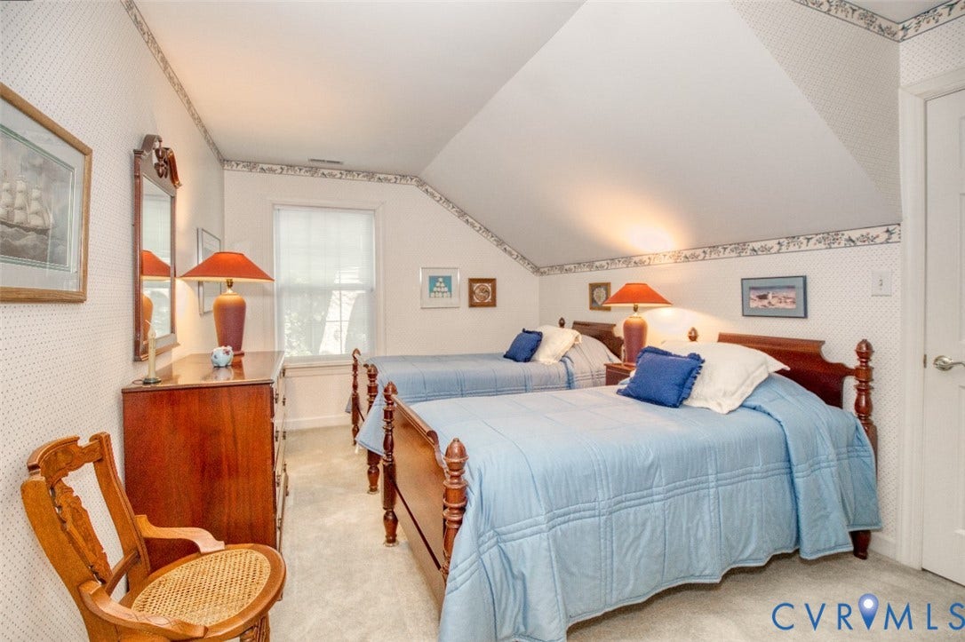 6311 Chiswick Park, Williamsburg, VA 23188 Charming second-floor bedroom featuring sloped vaulted ceilings with decorative trim, two twin beds with wooden posts, natural light from a front-facing window, warm wood-finish dresser, and coordinating table lamps with orange shades