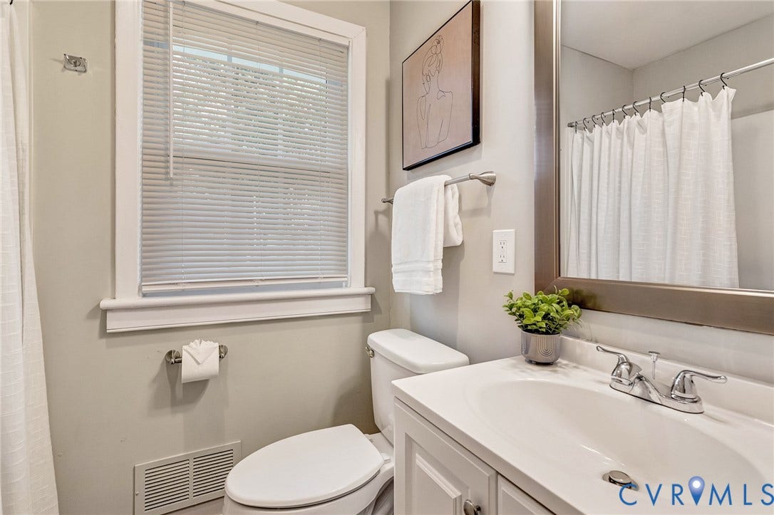 2807 Rothland Drive, Henrico, VA 23294 White vanity with an integrated sink and chrome faucet, large framed mirror, toilet with white trim window, and a shower with a white curtain