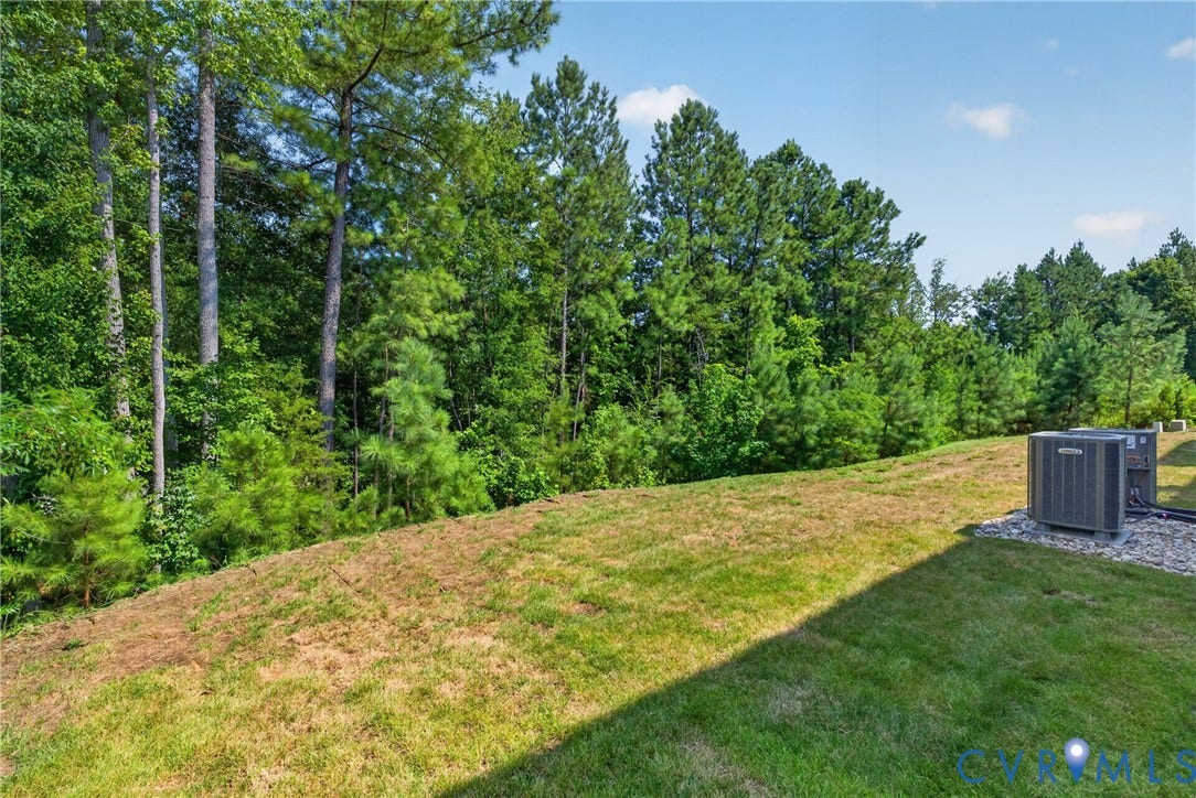6537 Hardee Haven Place, Midlothian, VA 23112 Expansive sloped lawn with a dense tree line backdrop, featuring two outdoor HVAC units on a gravel pad