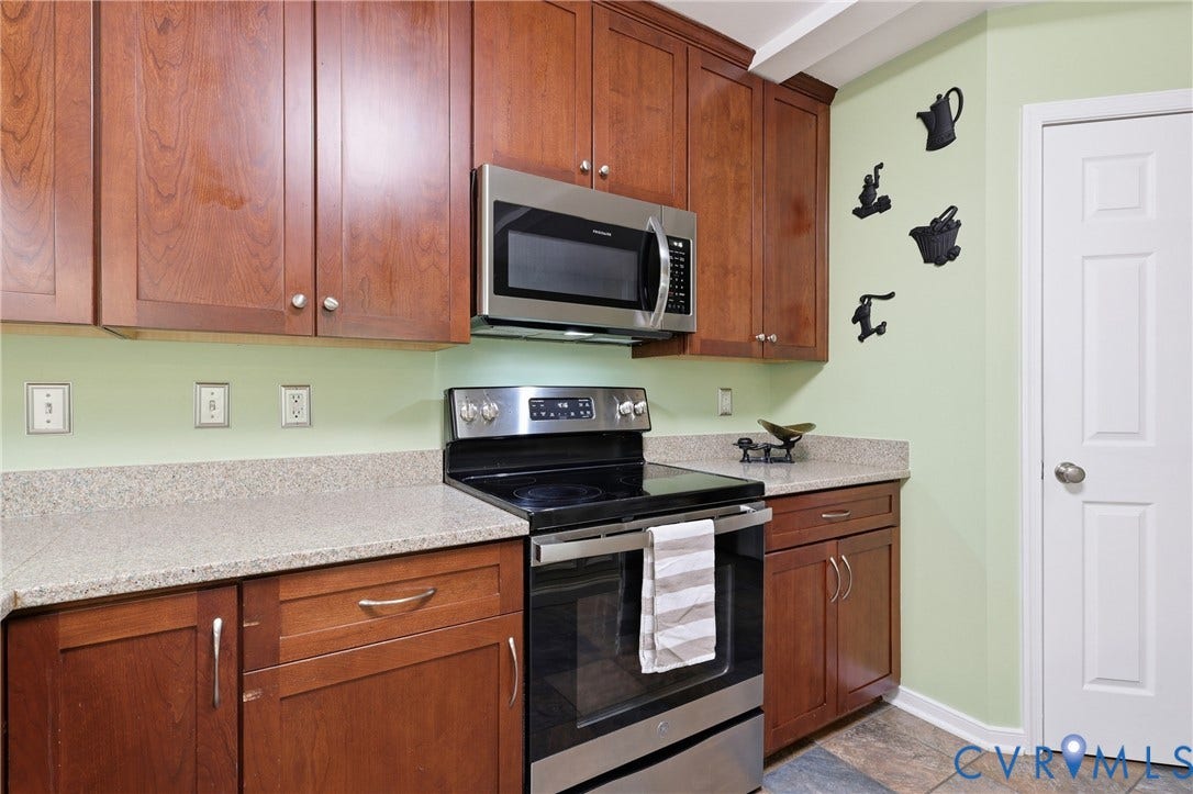 5295 Chimney Springs Drive, Saunders Acres, Goochland, VA 23063 Galley kitchen featuring warm wood cabinetry, stainless steel appliances including a slide-in range and over-the-range microwave, light stone countertops, soft green painted walls, and tile flooring