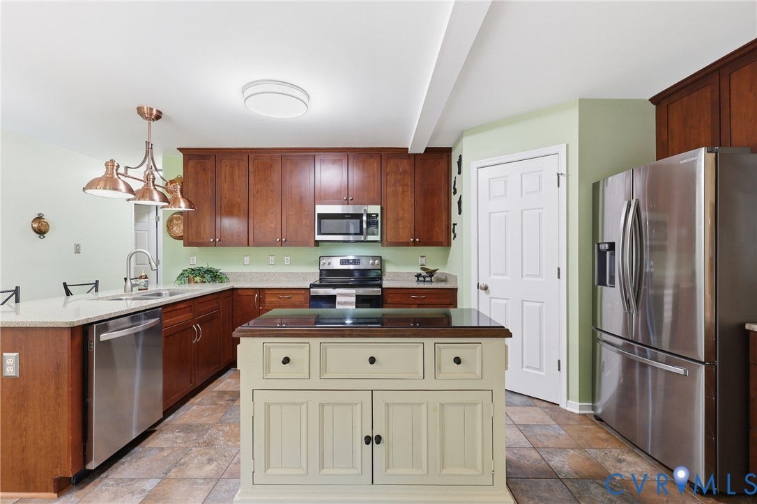 5295 Chimney Springs Drive, Saunders Acres, Goochland, VA 23063 Chef's kitchen featuring rich wood cabinetry, stainless steel appliances including a built-in microwave and refrigerator, a cream-painted island with storage and counter seating, ceramic tile flooring, and light green accent walls
