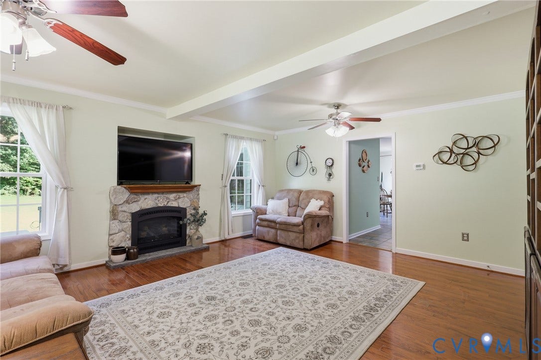 5295 Chimney Springs Drive, Saunders Acres, Goochland, VA 23063 Hardwood flooring, stone fireplace with hearth, white window trim, white crown molding, and two ceiling fans with light kits