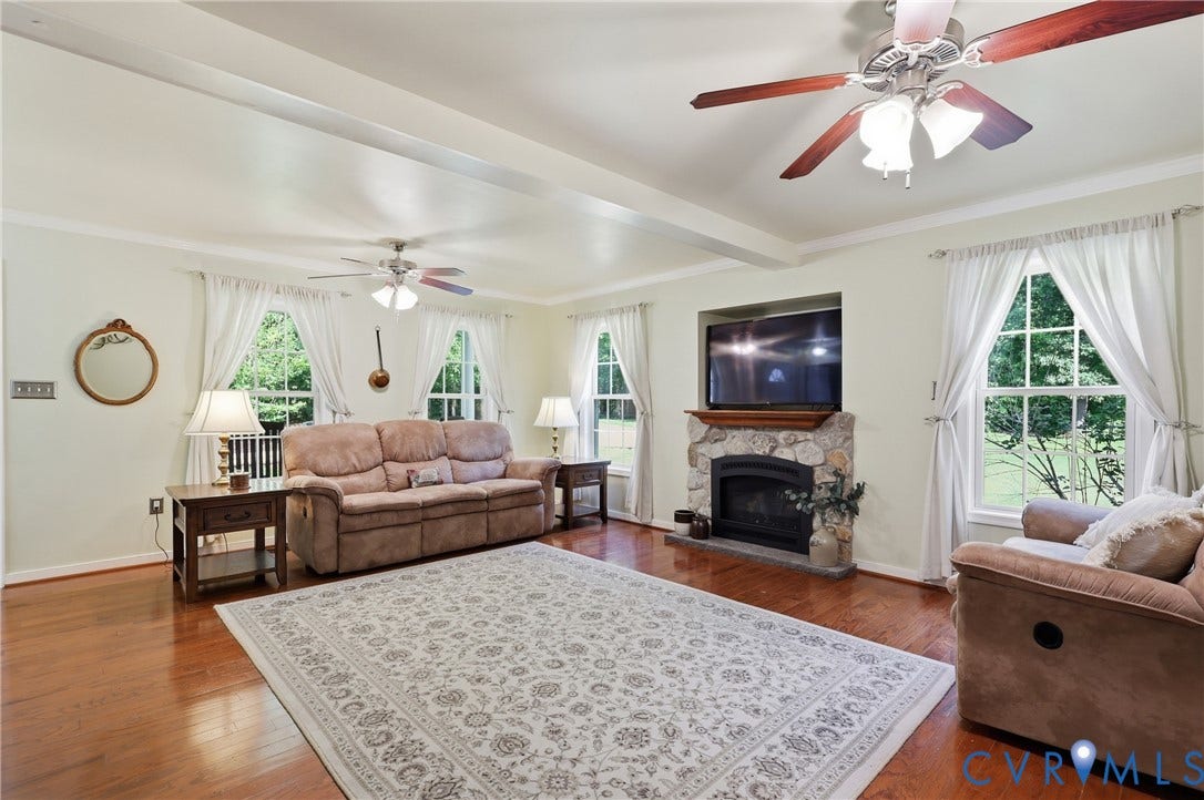5295 Chimney Springs Drive, Saunders Acres, Goochland, VA 23063 Hardwood flooring, stone-faced fireplace with wood mantel, tray ceiling, multiple ceiling fans with lighting, and several windows