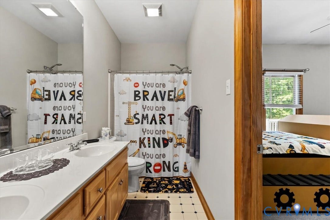 3060 Moyer Road, Powhatan, VA 23139 Bathroom featuring wood-finish vanity cabinetry with a white undermount sink, neutral tile flooring, and inspirational wall decals