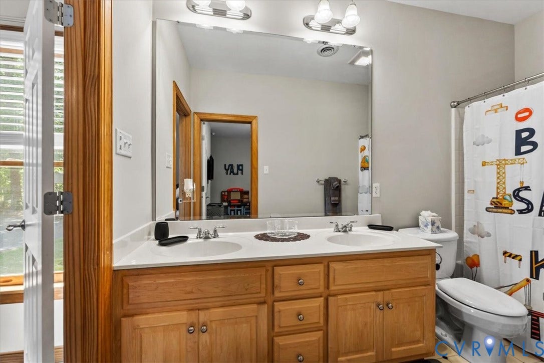 3060 Moyer Road, Powhatan, VA 23139 Spa-inspired bathroom featuring warm wood cabinetry with ample storage, a generous countertop with dual sink setup, and polished chrome fixtures