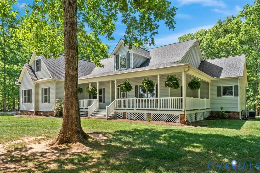 3060 Moyer Road, Powhatan, VA 23139 Classic farmhouse design featuring a welcoming front porch with white railings and decorative columns, light green exterior siding, multiple gabled rooflines with architectural dormers, and a mature shade tree anchoring the manicured front lawn