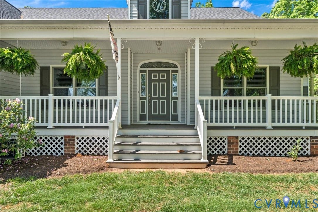 3060 Moyer Road, Powhatan, VA 23139 Classic front elevation featuring a welcoming covered porch with white railings, dual hanging planters, paneled entry door with sidelights, and brick foundation skirt with lattice detailing