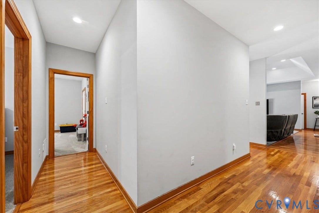 3060 Moyer Road, Powhatan, VA 23139 Modern hallway showcasing warm wood-finish flooring, white walls, recessed ceiling lighting, and wood-trimmed doorways
