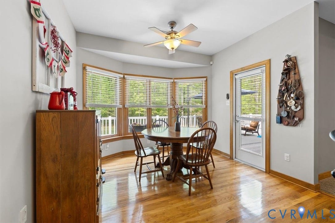 3060 Moyer Road, Powhatan, VA 23139 Bright sunroom with expansive glass-pane doors and windows framing outdoor scenery, warm wood-finish flooring, ceiling fan with integrated lighting, and rich wood cabinetry