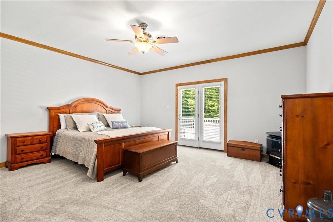 3060 Moyer Road, Powhatan, VA 23139 Spacious primary bedroom featuring hardwood furnishings, vaulted ceiling with crown molding and ceiling fan, light wood-finish flooring, and glass French doors opening to a private balcony with tree-line views