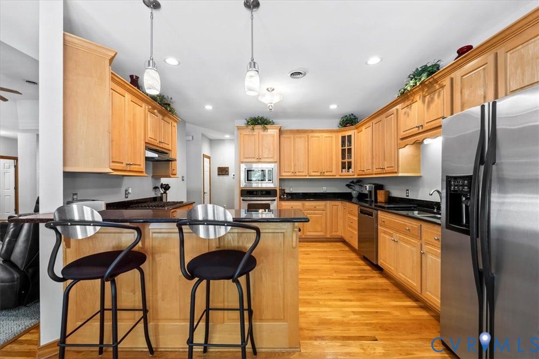 3060 Moyer Road, Powhatan, VA 23139 Chef's kitchen featuring warm wood cabinetry throughout, black granite countertops, stainless steel appliances including a side-by-side refrigerator, and a large center island with seating