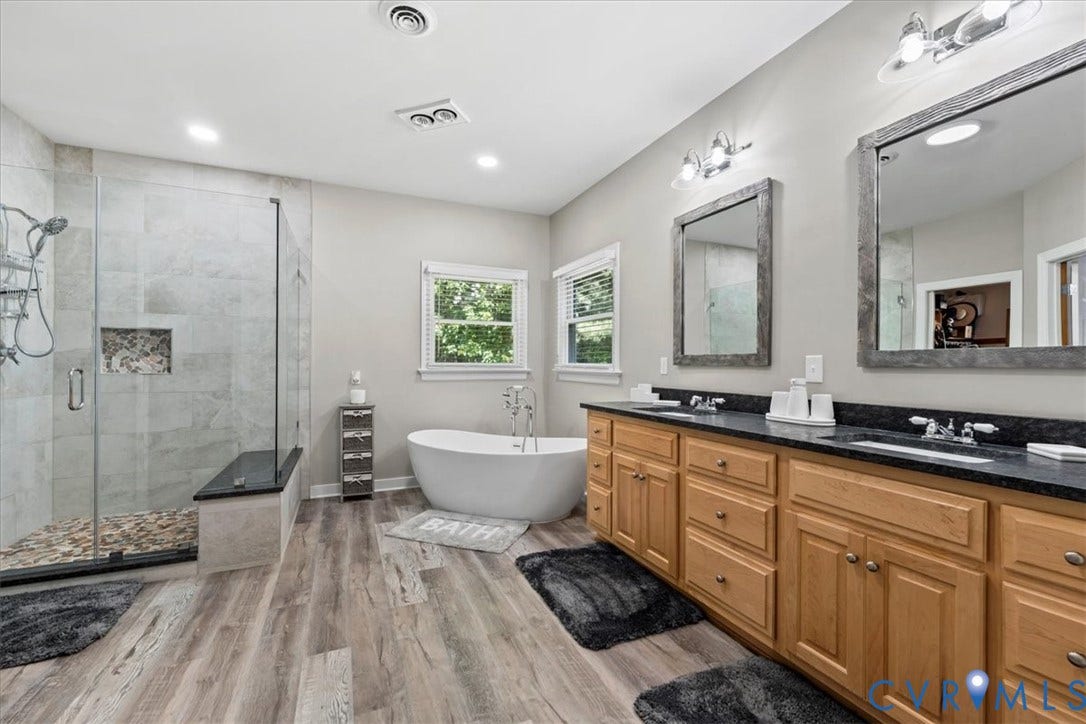 3060 Moyer Road, Powhatan, VA 23139 Spacious bathroom with wood-finish flooring, a freestanding soaking tub, a large glass-enclosed shower with a built-in bench, and a dual vanity with dark countertops