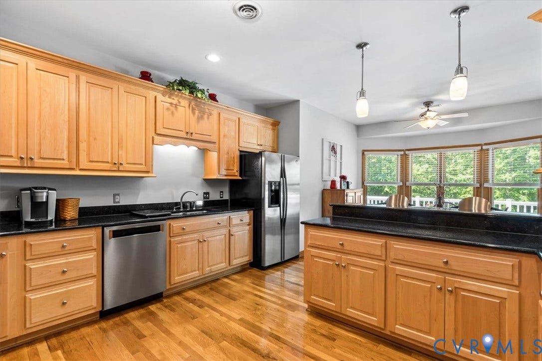 3060 Moyer Road, Powhatan, VA 23139 Kitchen featuring wood cabinetry, stainless steel appliances, black countertops, wood-finish flooring, and a bay window