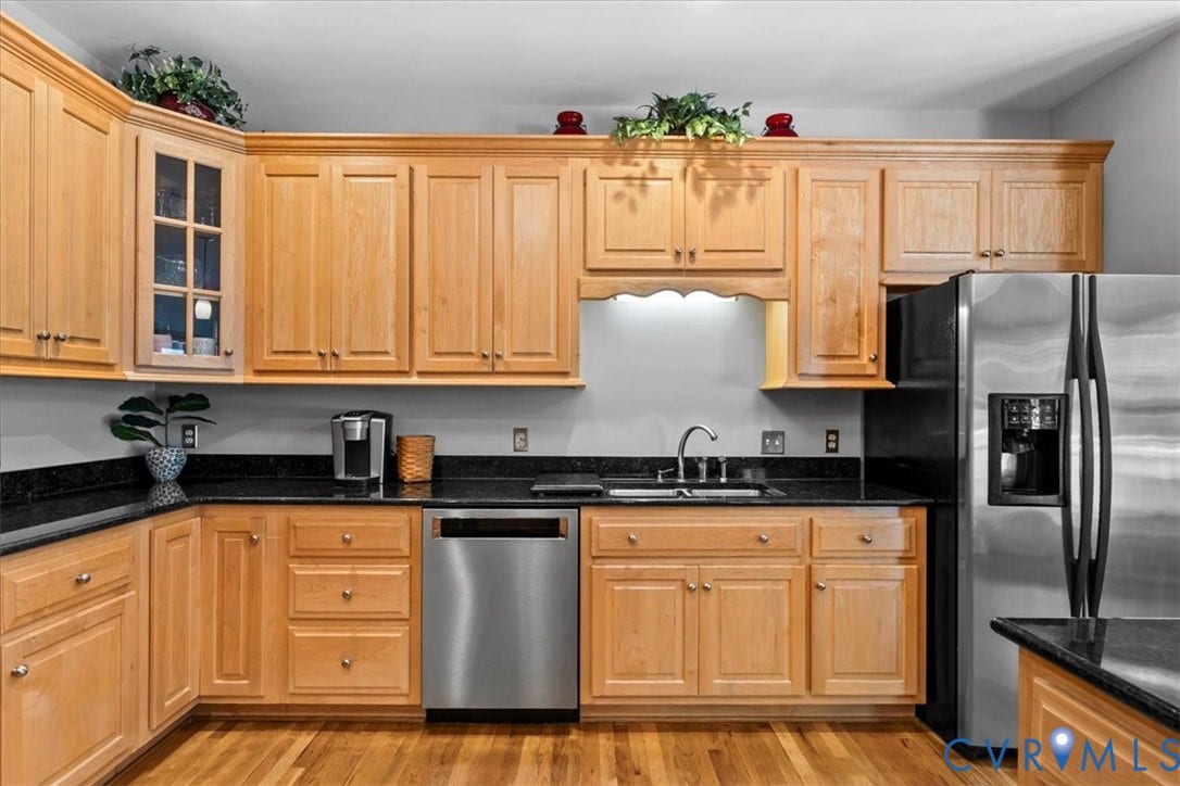 3060 Moyer Road, Powhatan, VA 23139 Chef's kitchen featuring warm wood cabinetry with raised-panel doors, stainless steel appliances including a French-door refrigerator and dishwasher, black quartz countertops, and a functional layout with ample storage