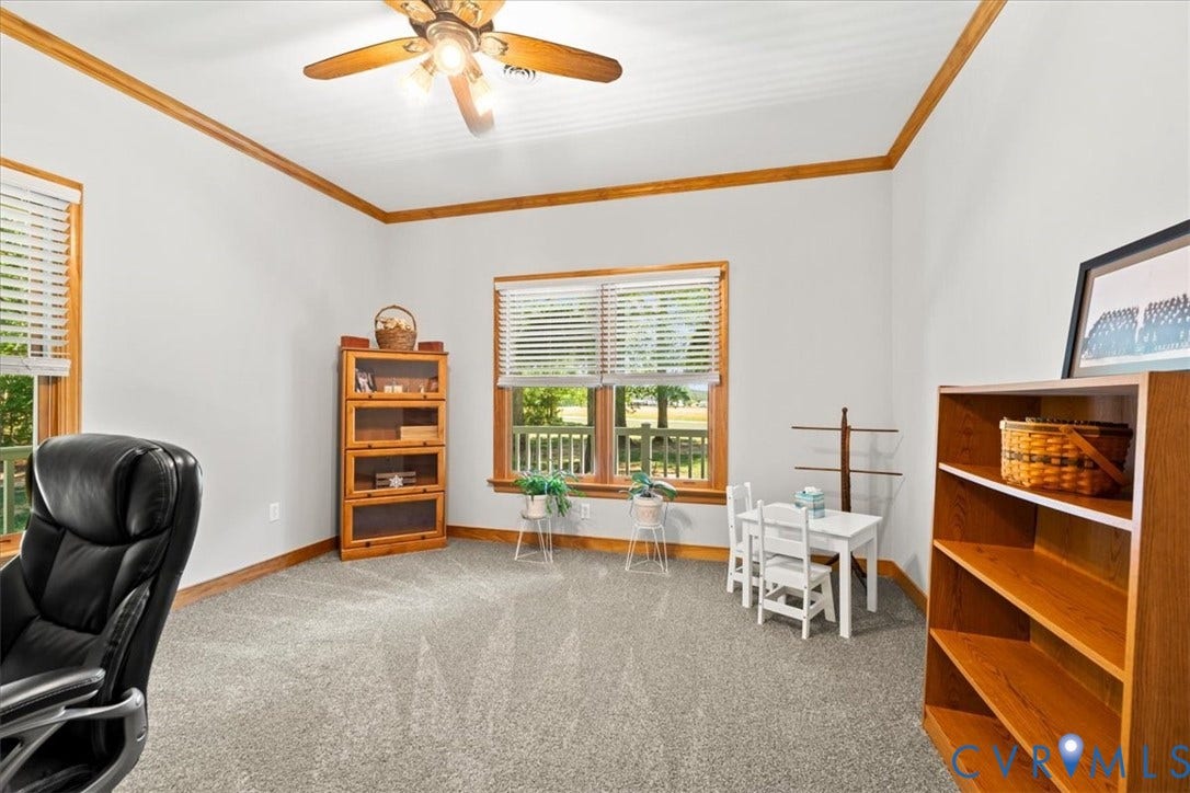 3060 Moyer Road, Powhatan, VA 23139 Bright, versatile room featuring wood-trimmed tray ceiling, ceiling fan with integrated lighting, expansive windows with wood-frame shutters offering natural light, built-in wood cabinetry with open shelving, and neutral carpeting throughout