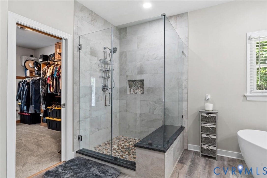 3060 Moyer Road, Powhatan, VA 23139 Spa-inspired primary bathroom featuring a frameless glass-enclosed shower with marble-look tile surround, rainfall showerhead, and river rock accent flooring