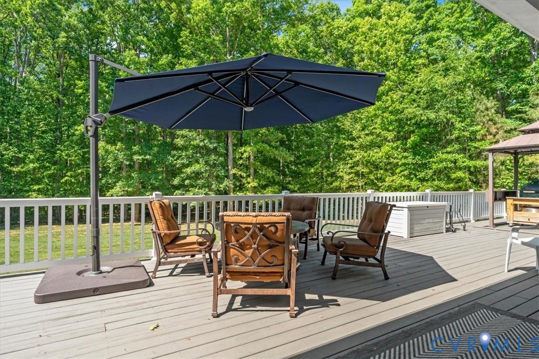 3060 Moyer Road, Powhatan, VA 23139 Expansive composite deck with mature tree canopy backdrop, featuring a cantilever umbrella with integrated base and multiple seating areas ideal for outdoor entertaining and relaxation